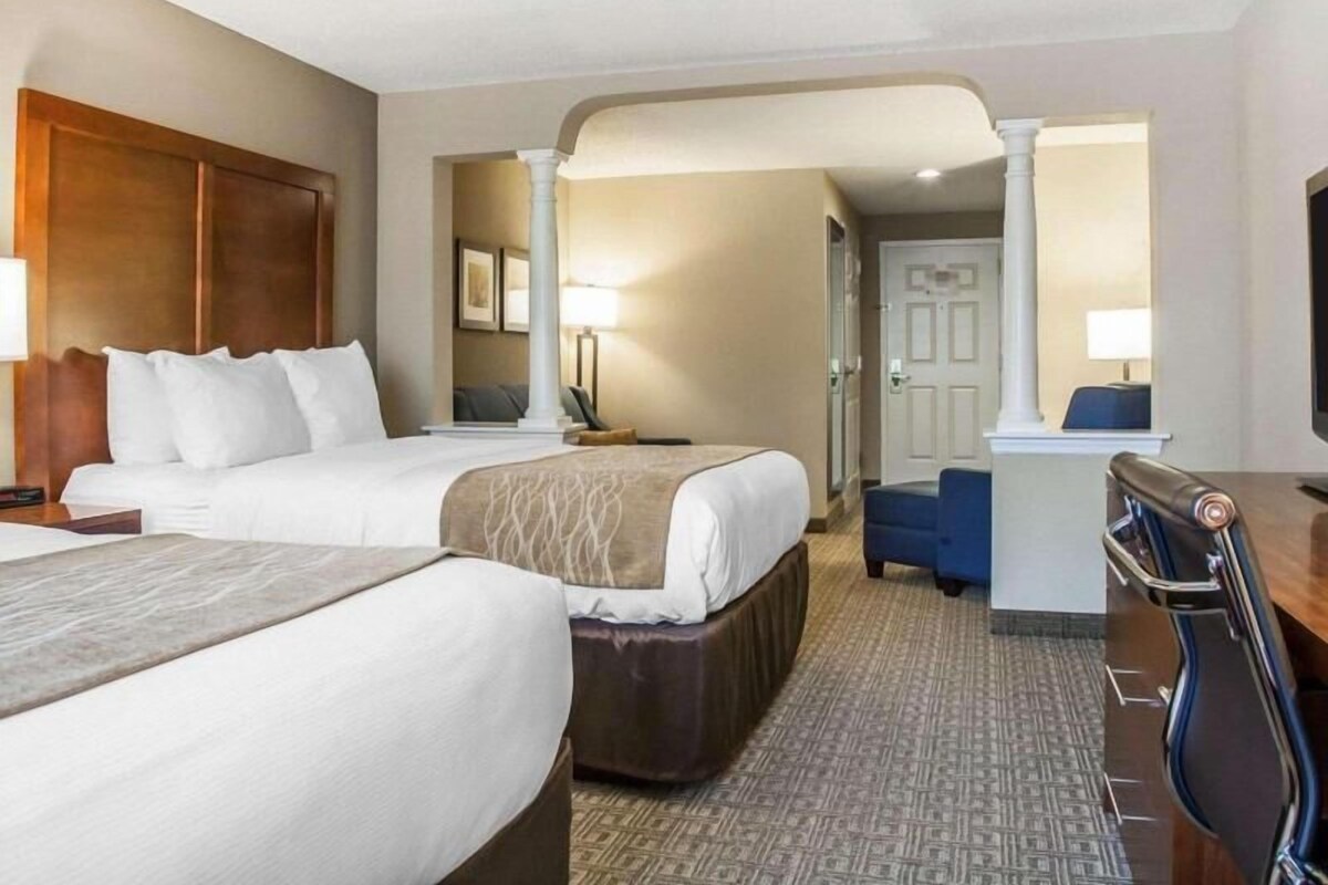 A hotel room with two beds, a desk, a chair, and a door leading to another room.