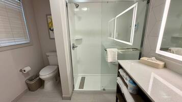 Un baño moderno con cabina de ducha de vidrio, inodoro y tocador con espejo.