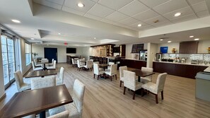 A hotel dining area with multiple tables and chairs, a bar, and a television screen. - Comfort Inn & Suites Sturbridge - Brimfield (Sturbridge)