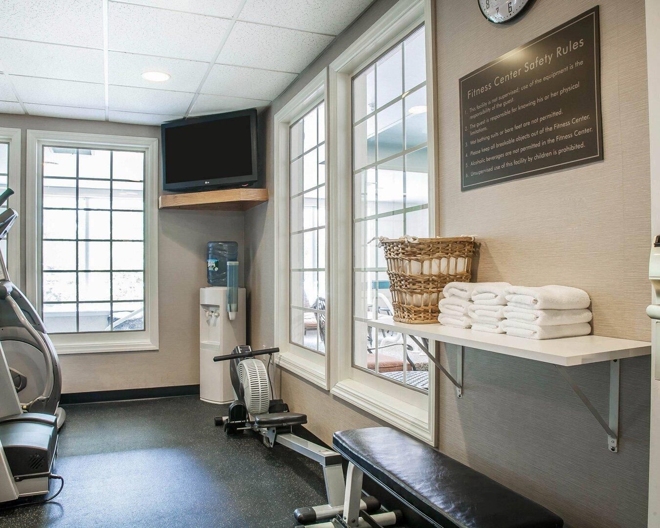 A fitness center with exercise equipment, a water dispenser, a TV, and a sign listing safety rules.