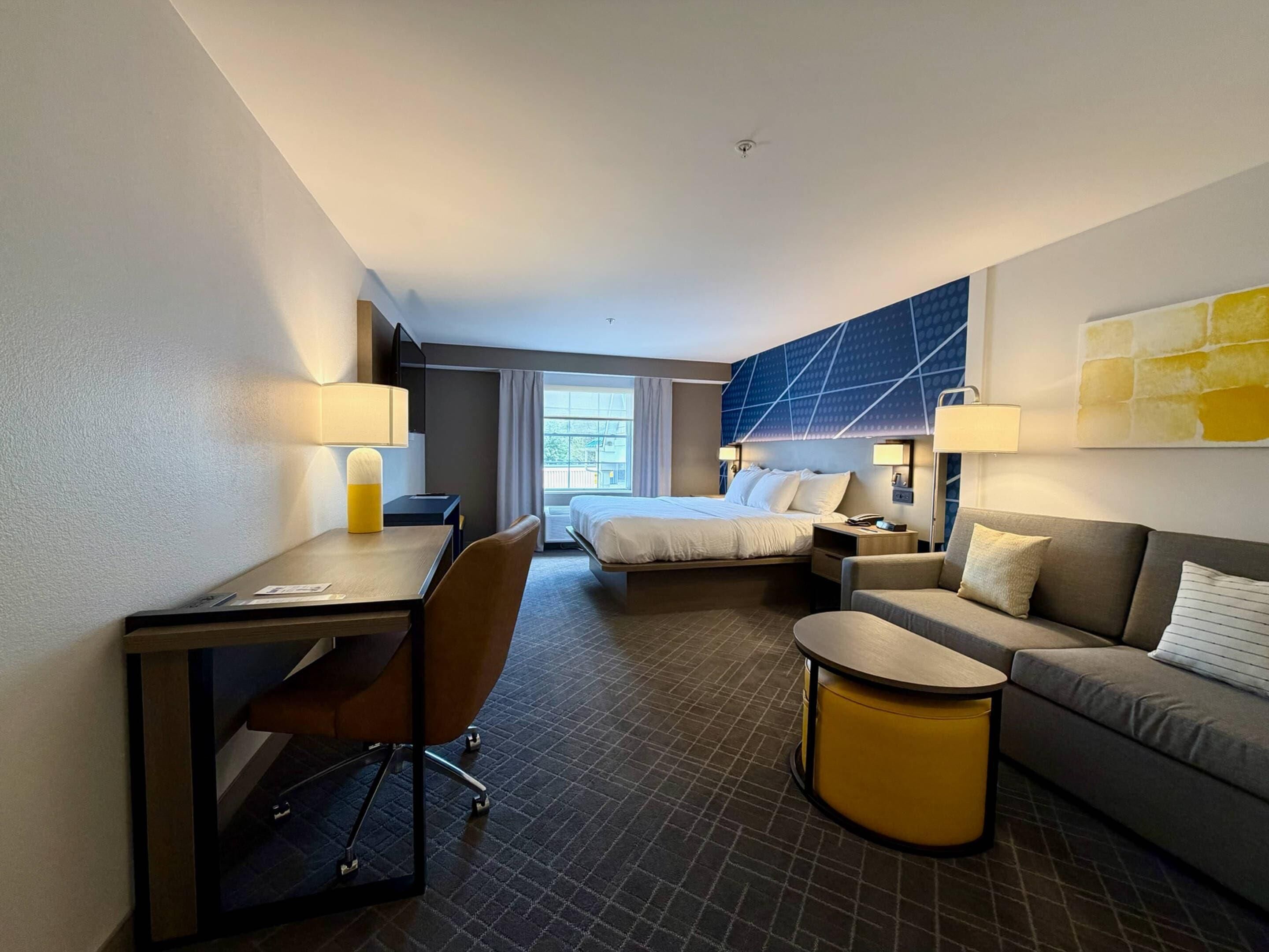 A hotel room with a bed, a desk, a chair, a sofa, and a small table.