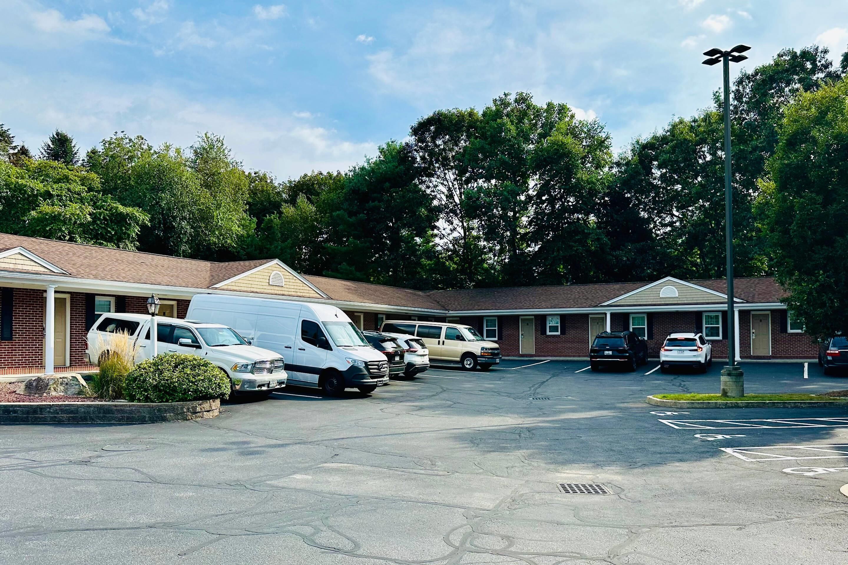 A parking lot with several vehicles, including vans and cars, and a building with a brick facade and a flat roof.