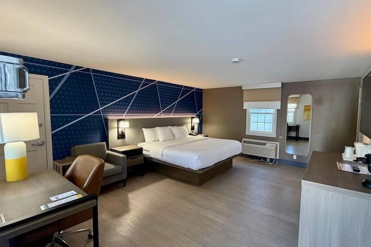 A hotel room with a bed, desk, chair, bedside tables, a TV, and a wall with geometric patterns.