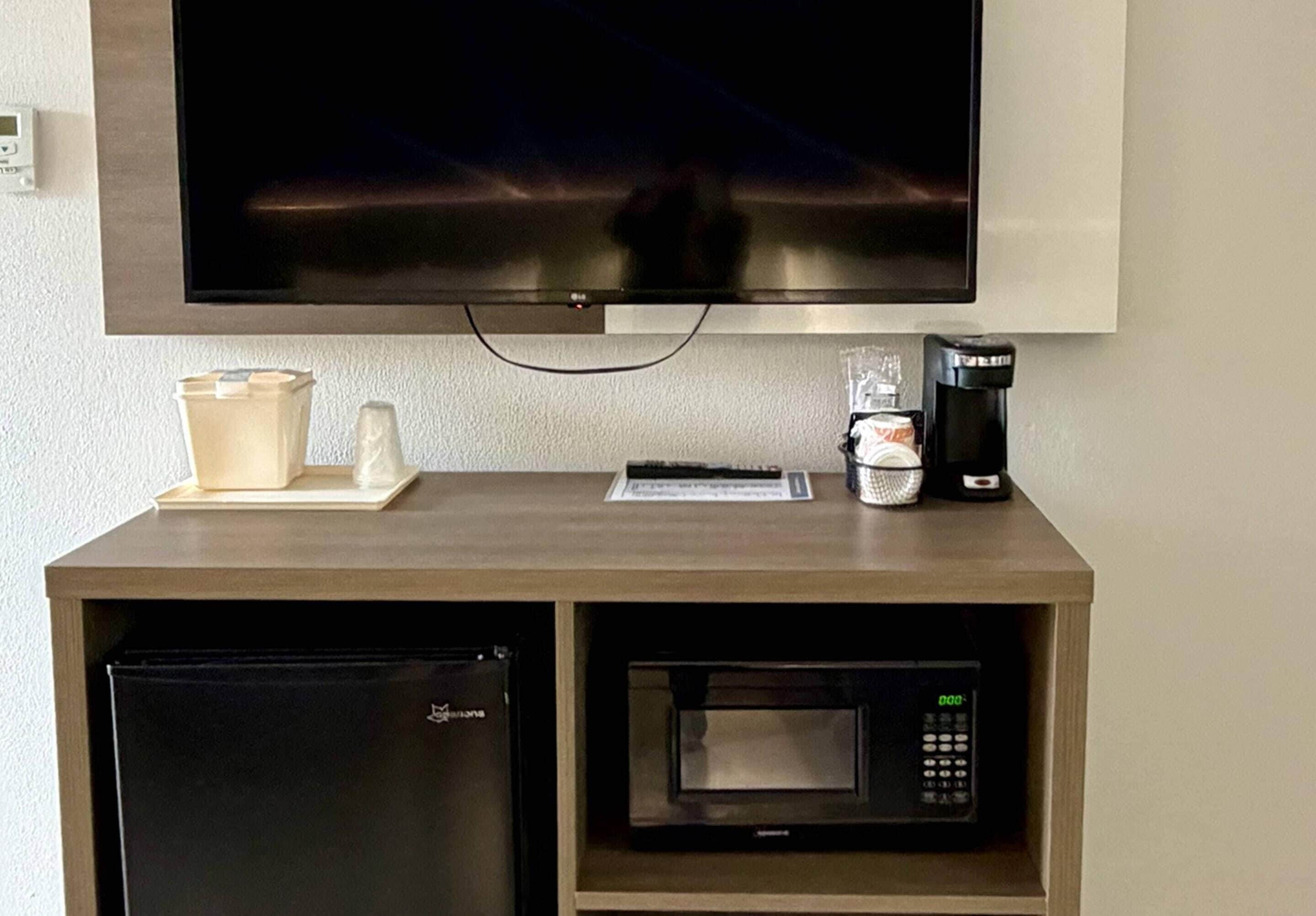 A kitchenette with a microwave, a coffee maker, a refrigerator, and a flat-screen TV mounted above the counter.
