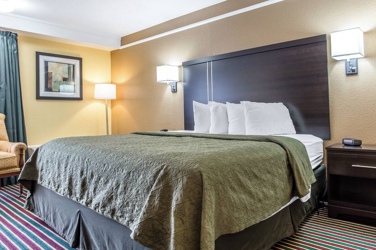 A hotel room with a large bed, a bedside table, a lamp, and a chair.