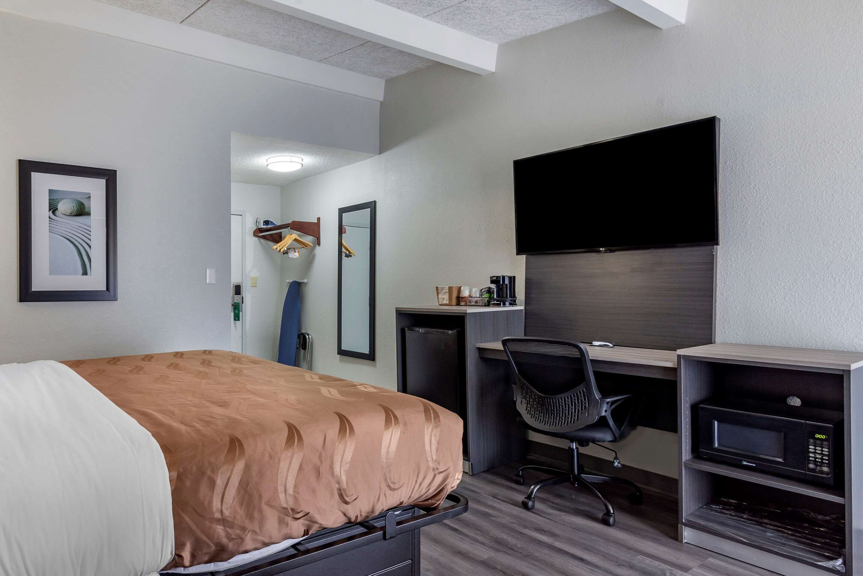 Een hotelkamer met een bed, een bureau, een stoel, een flatscreen televisie en een magnetron.