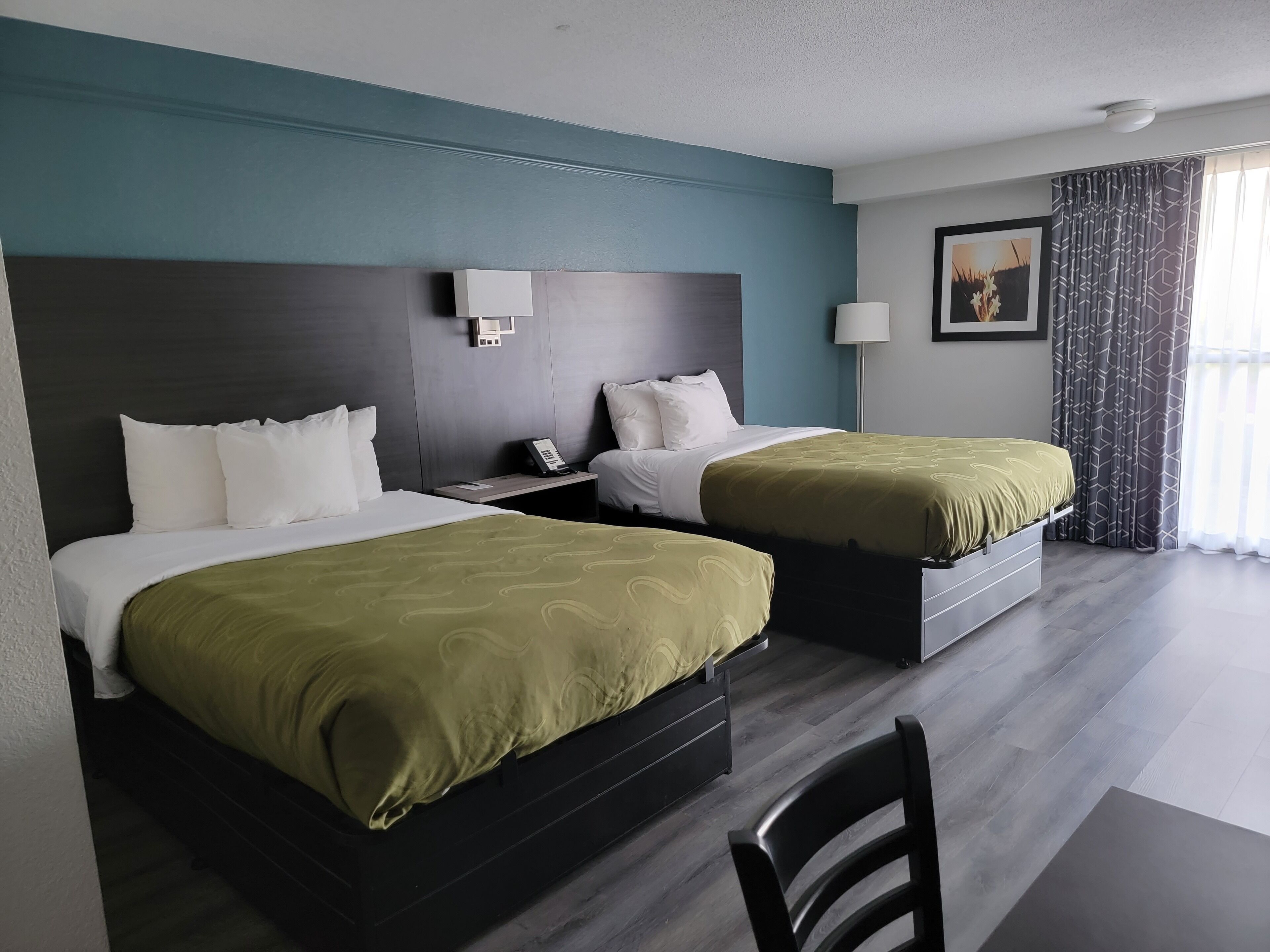 A hotel room with two beds, a desk, a chair, a phone, and a painting on the wall.