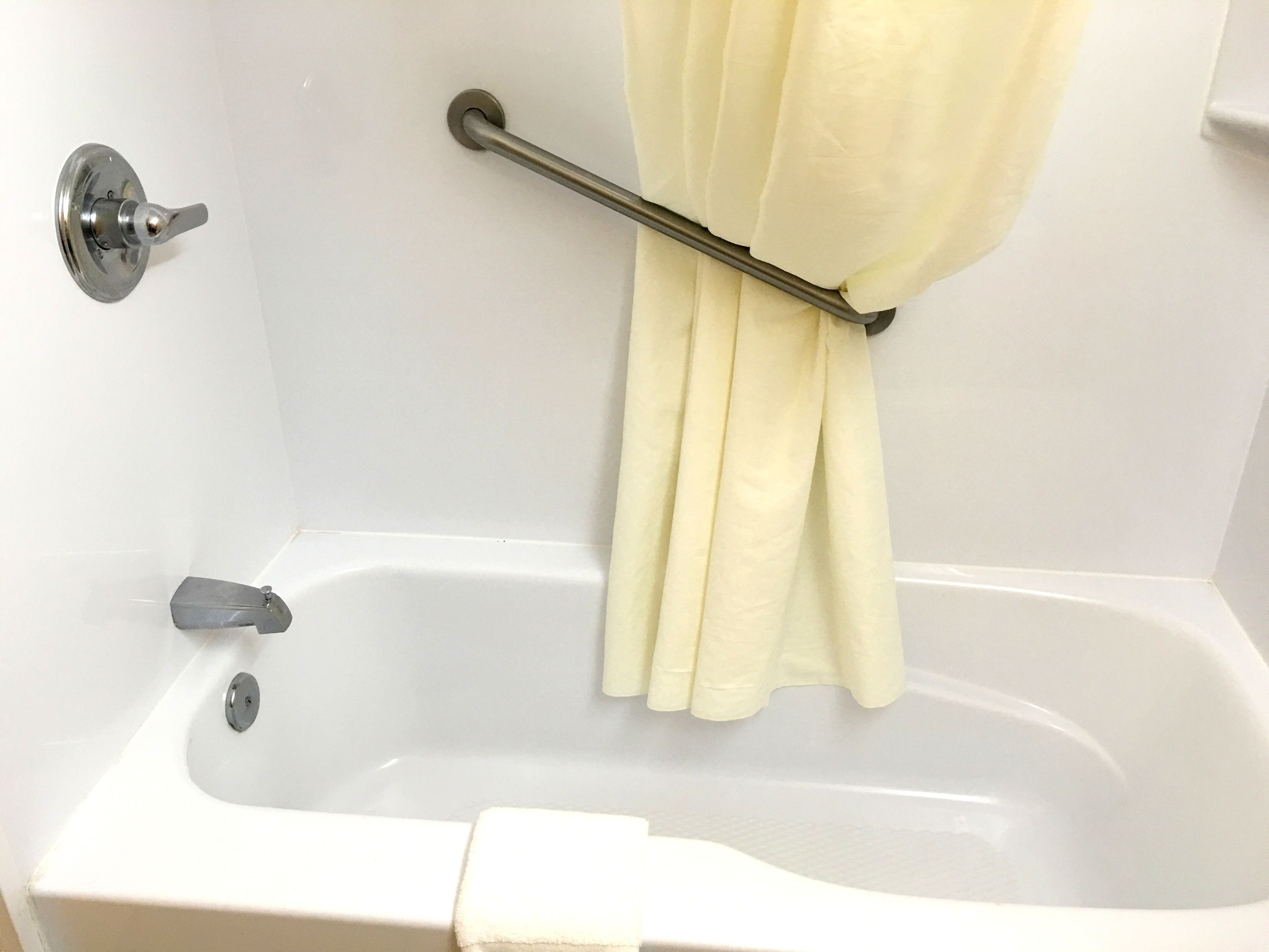 A white bathtub with a shower curtain rod and a towel.