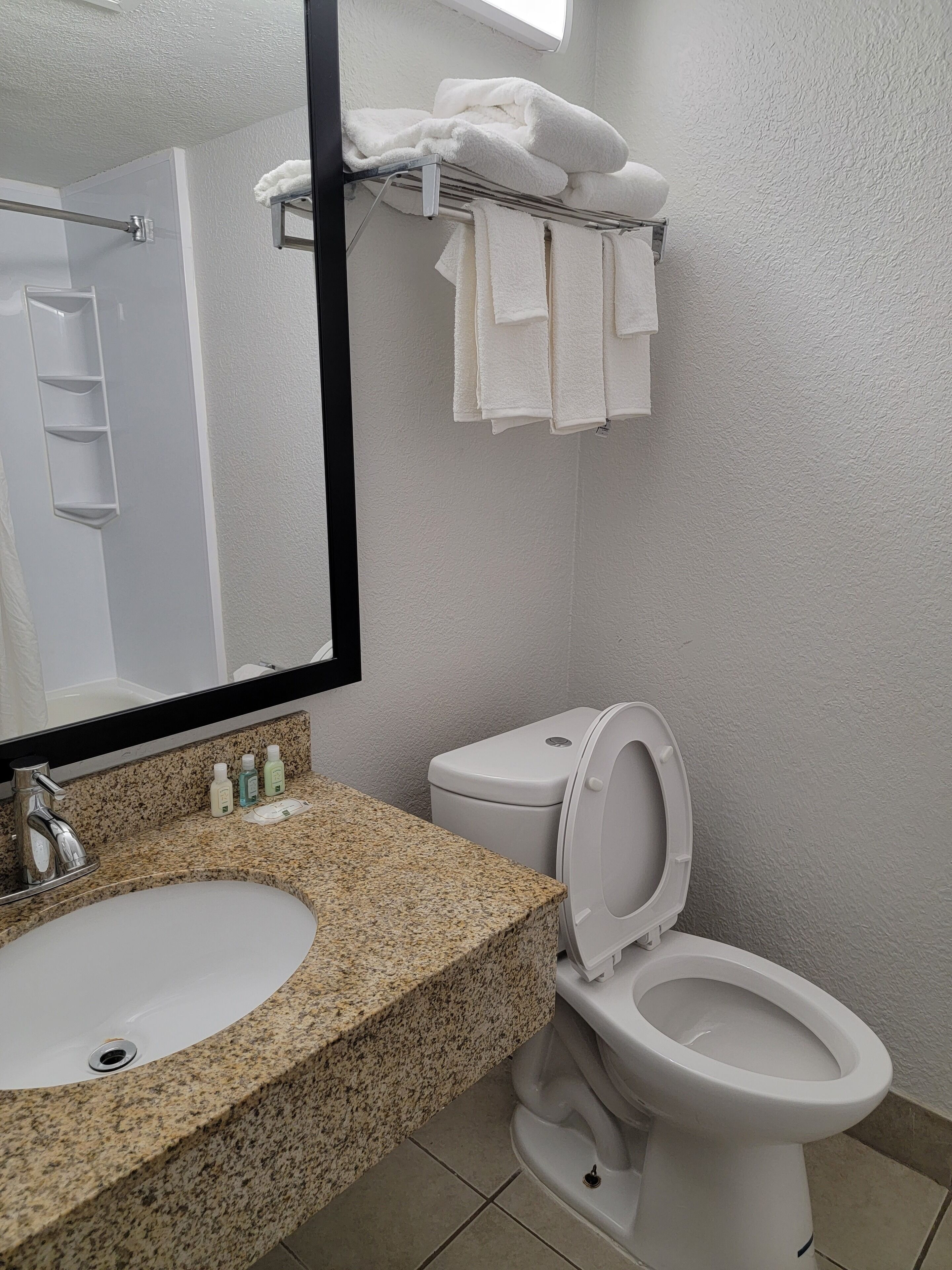 A bathroom with a granite countertop sink, a white toilet, and a towel rack with folded towels.