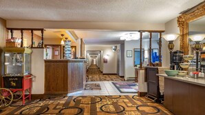 A hotel lobby with a wooden reception desk, a red cart, a patterned carpet, and a hallway leading to the rooms. - Quality Inn Saint Ignace I-75 (St Ignace)