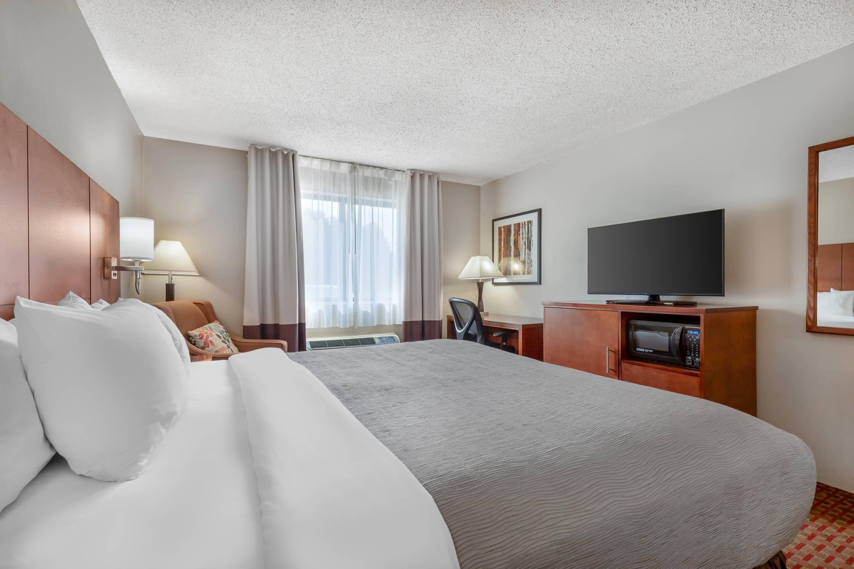 A hotel room with a large bed, a desk with a chair, a television, and a microwave.