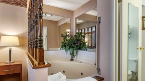 A bathroom with a large bathtub, a wooden staircase, a mirror, and a vase with flowers. - Quality Inn Saint Ignace I-75 (St Ignace)
