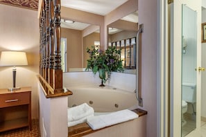 Un baño con una bañera grande, una escalera de madera, un espejo y un florero con flores.