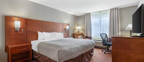 A hotel room with a large bed, a desk, a chair, a television, and a window with curtains.