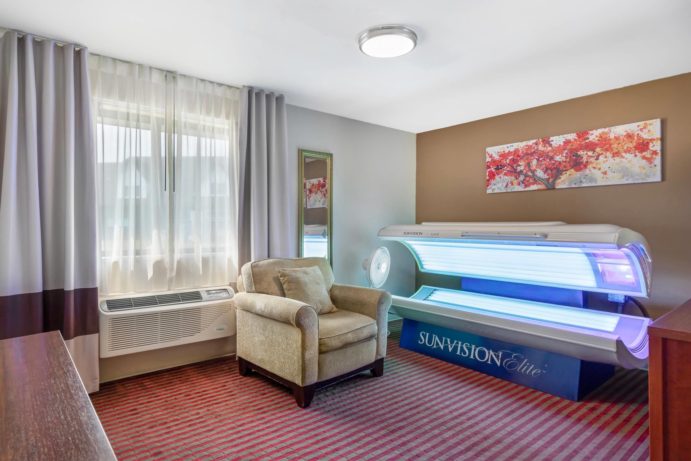 A hotel room with a massage chair, a wall-mounted massage table, and a large window with curtains.