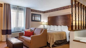 A hotel room with a bed, a sofa, a small table, a lamp, and a staircase. - Quality Inn Saint Ignace I-75 (St Ignace)