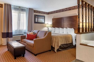Una habitación de hotel con cama, sofá, una mesita, lámpara y una escalera.