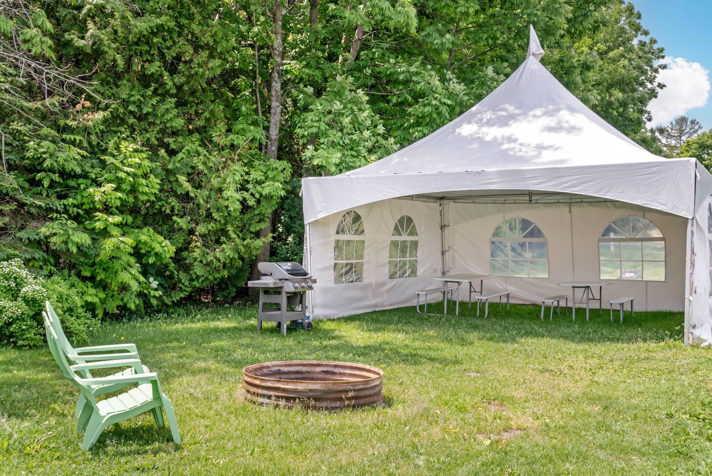 Una carpa con una mesa y sillas dispuestas en un área con césped y árboles al fondo.