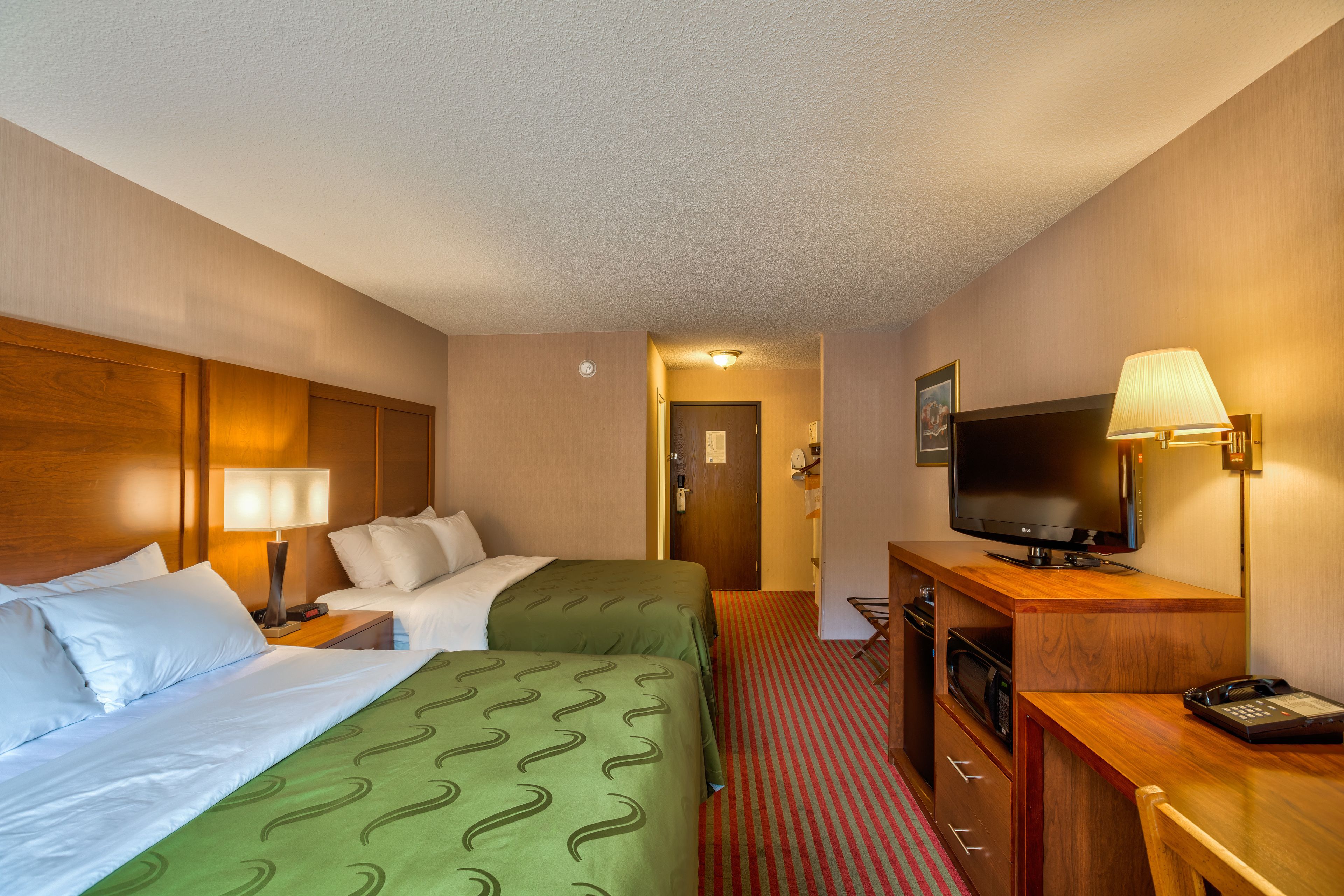 Habitación de hotel con dos camas, un escritorio, televisión, lámpara y microondas.