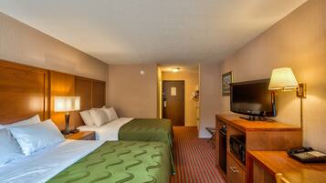 Ein Hotelzimmer mit zwei Betten, einem Schreibtisch mit Fernseher, einer Lampe und einer Mikrowelle.