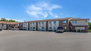 A multi-story hotel with a parking lot, several vehicles, and a clear blue sky. - Quality Inn Saint Ignace I-75 (St Ignace)