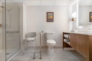 Un baño moderno con cabina de ducha de vidrio, un inodoro, una silla con bandeja y un tocador de madera con espejo.