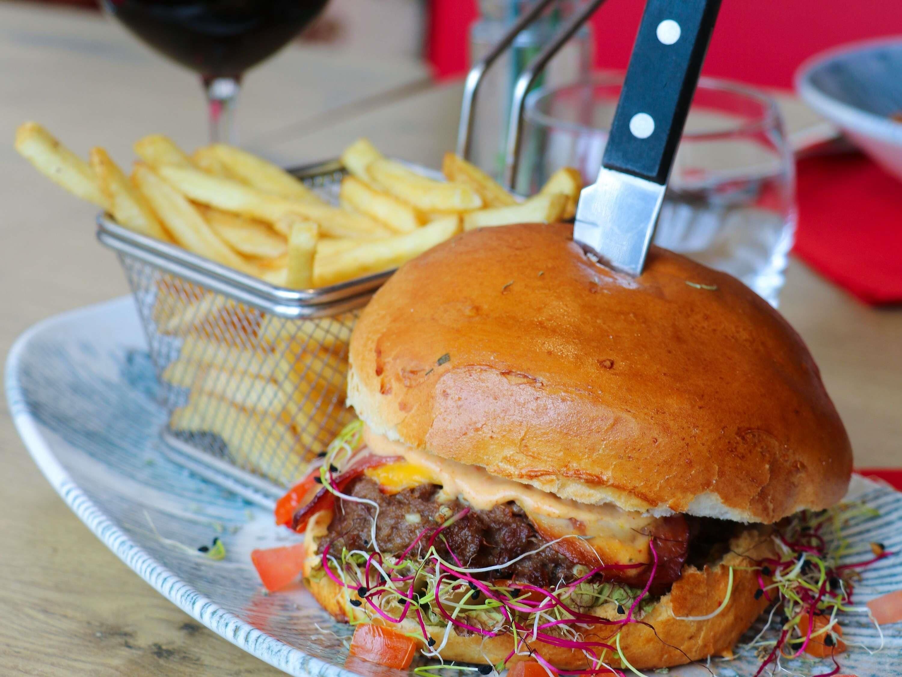 A sandwich with a bun, fries, and a knife.