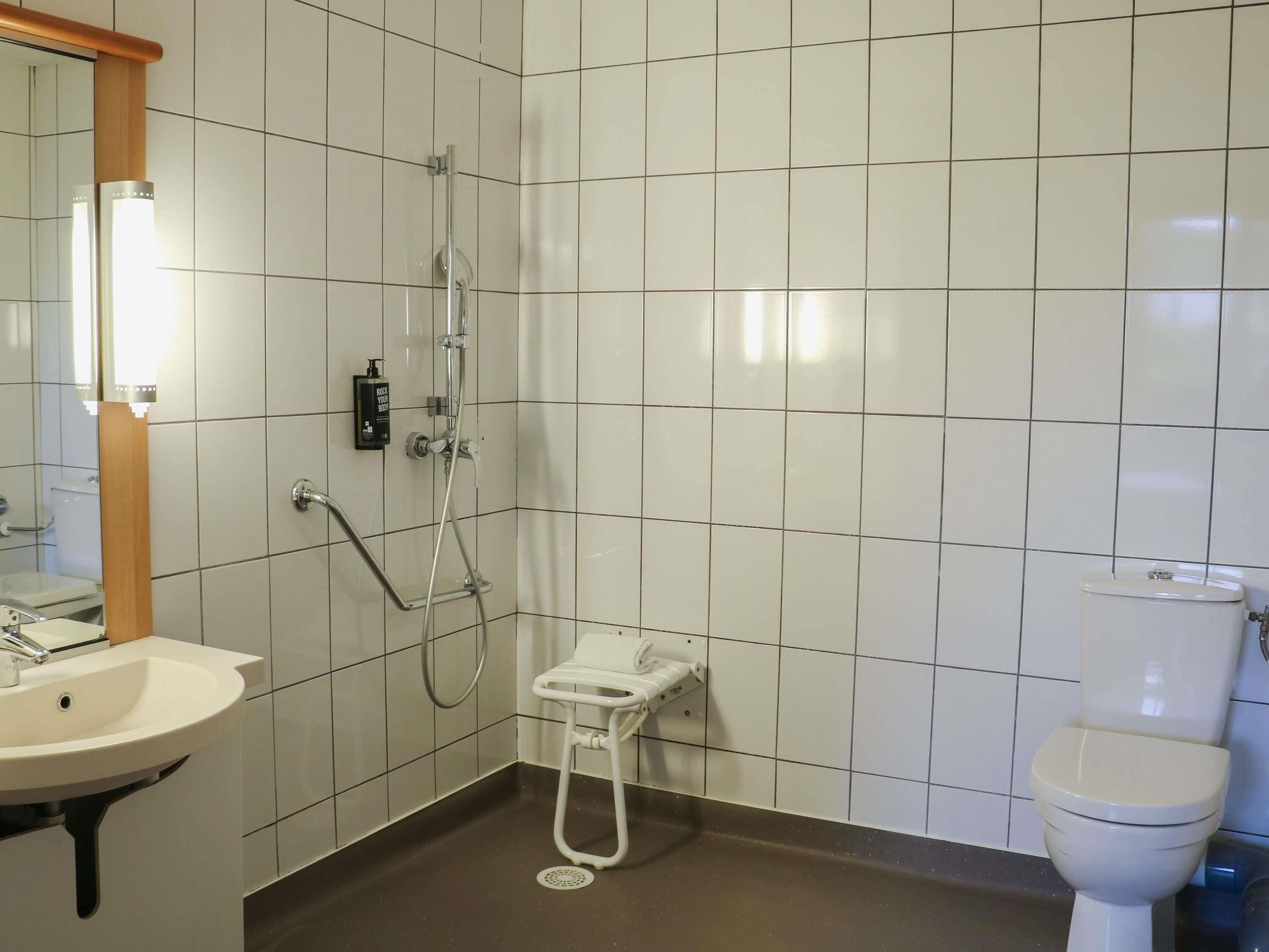Een badkamer met witte betegelde wanden, een wastafel, een toilet en een douche met een handdouche.