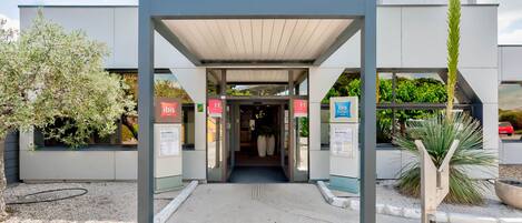 A modern hotel entrance with a covered walkway, a reception desk, and a sign indicating a budget hotel.