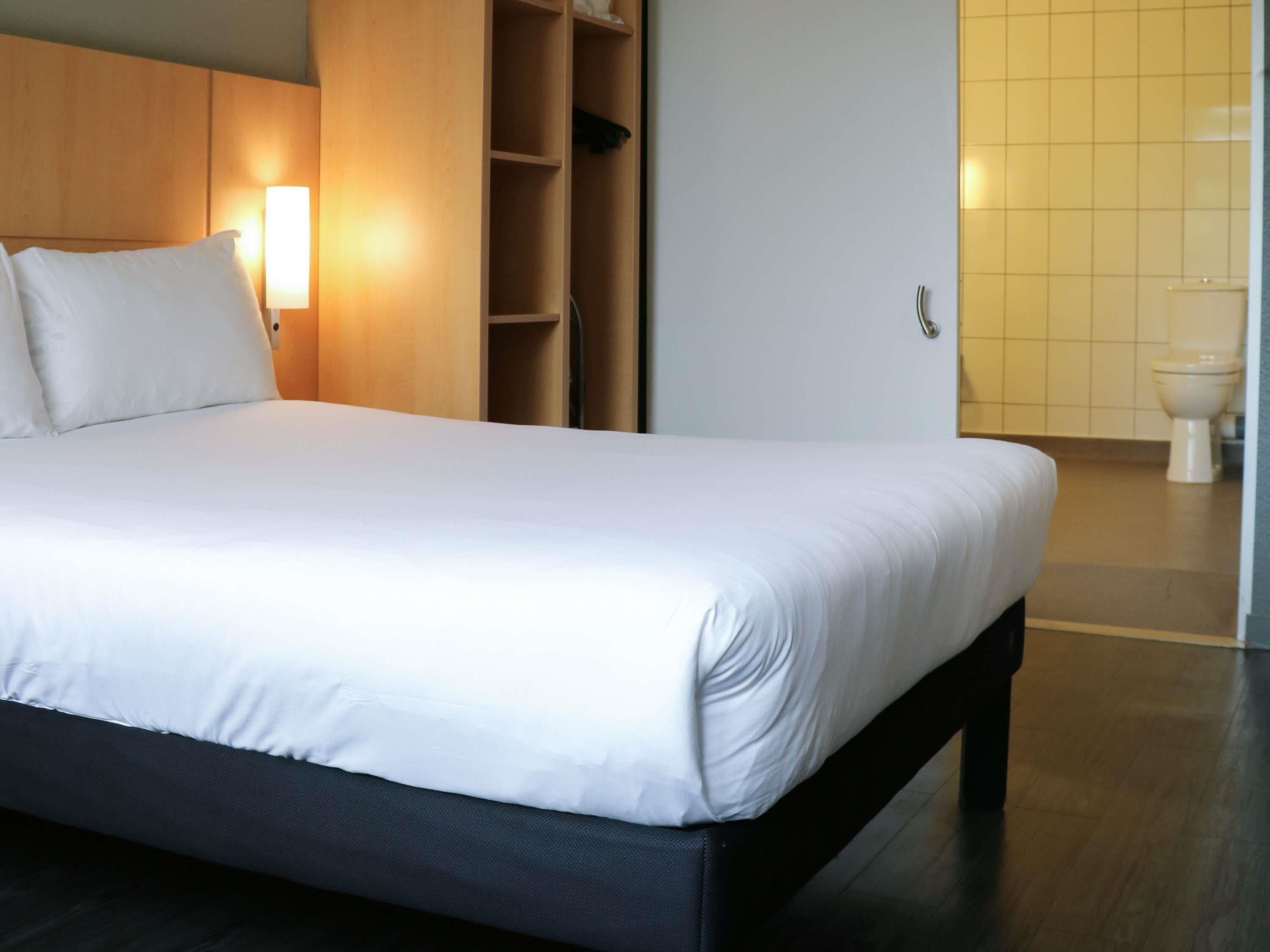 A hotel room with a large bed, a wardrobe, a bedside table, and a bathroom with a toilet.