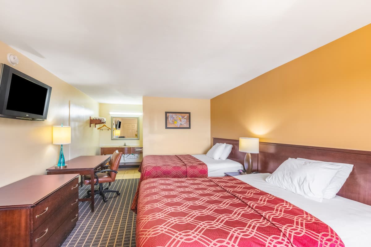 A hotel room with two beds, a desk, a chair, a TV, and a bathroom visible in the background.