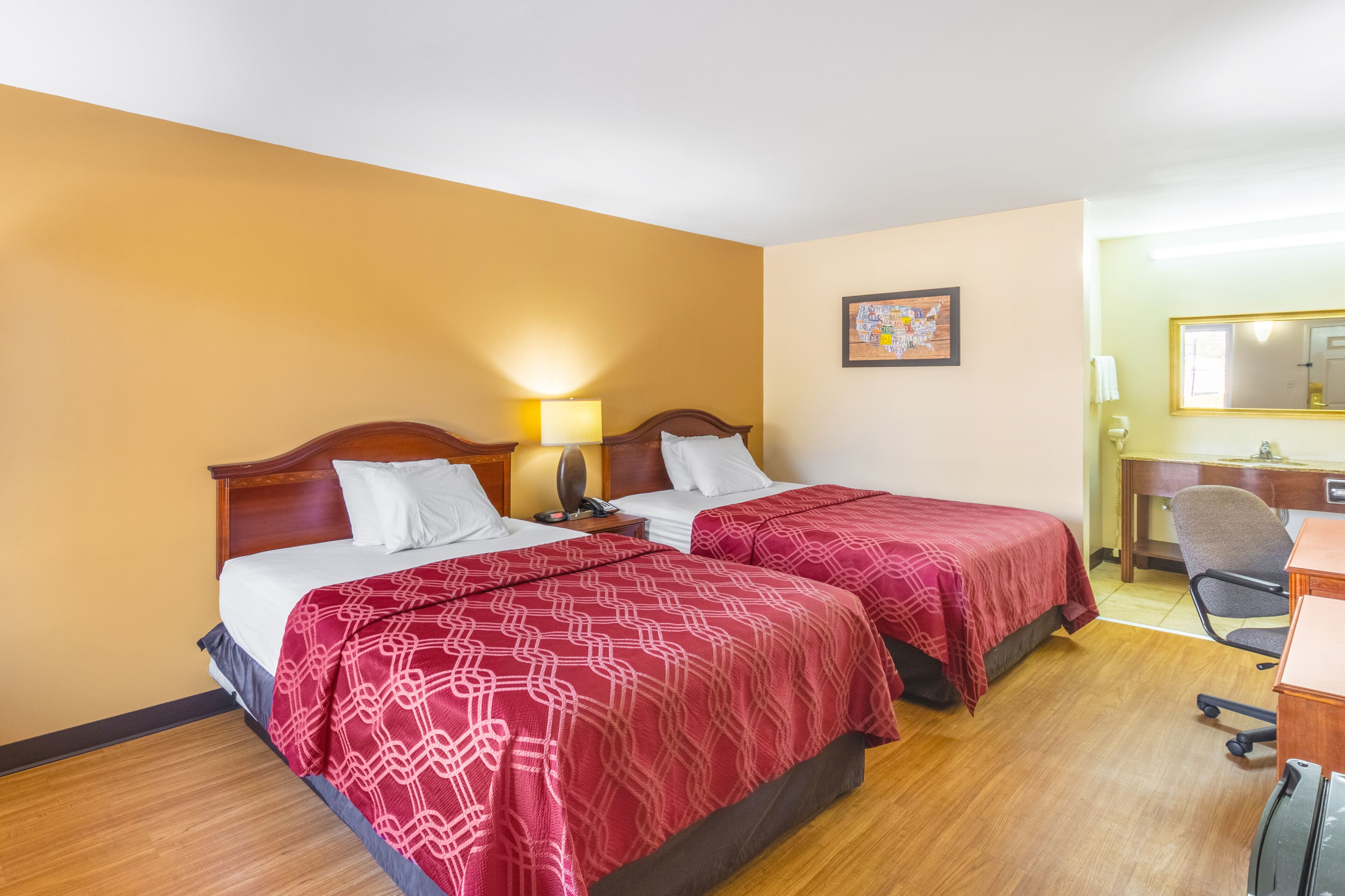 A hotel room with two beds, a desk, a chair, and a mirror.