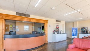 A reception area with a curved desk, a coffee station, and a seating area with a red sofa. - Econo Lodge Gaffney (Gaffney)