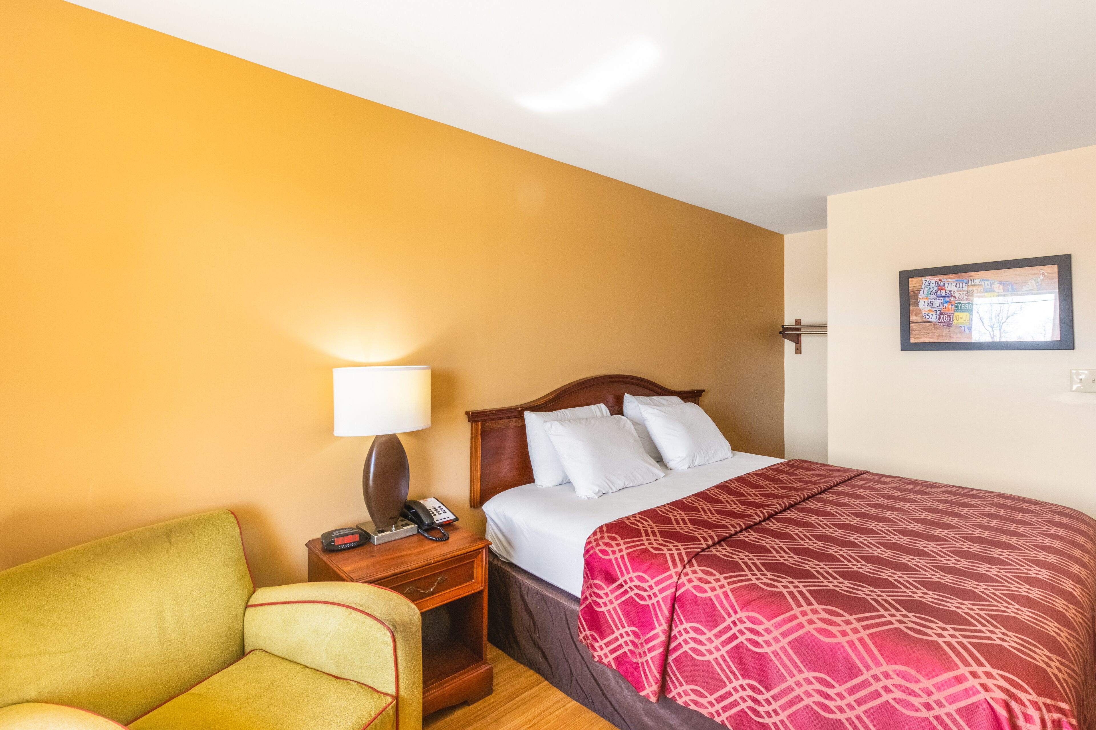 Habitación de hotel con cama, mesita de noche con lámpara, teléfono y una silla.