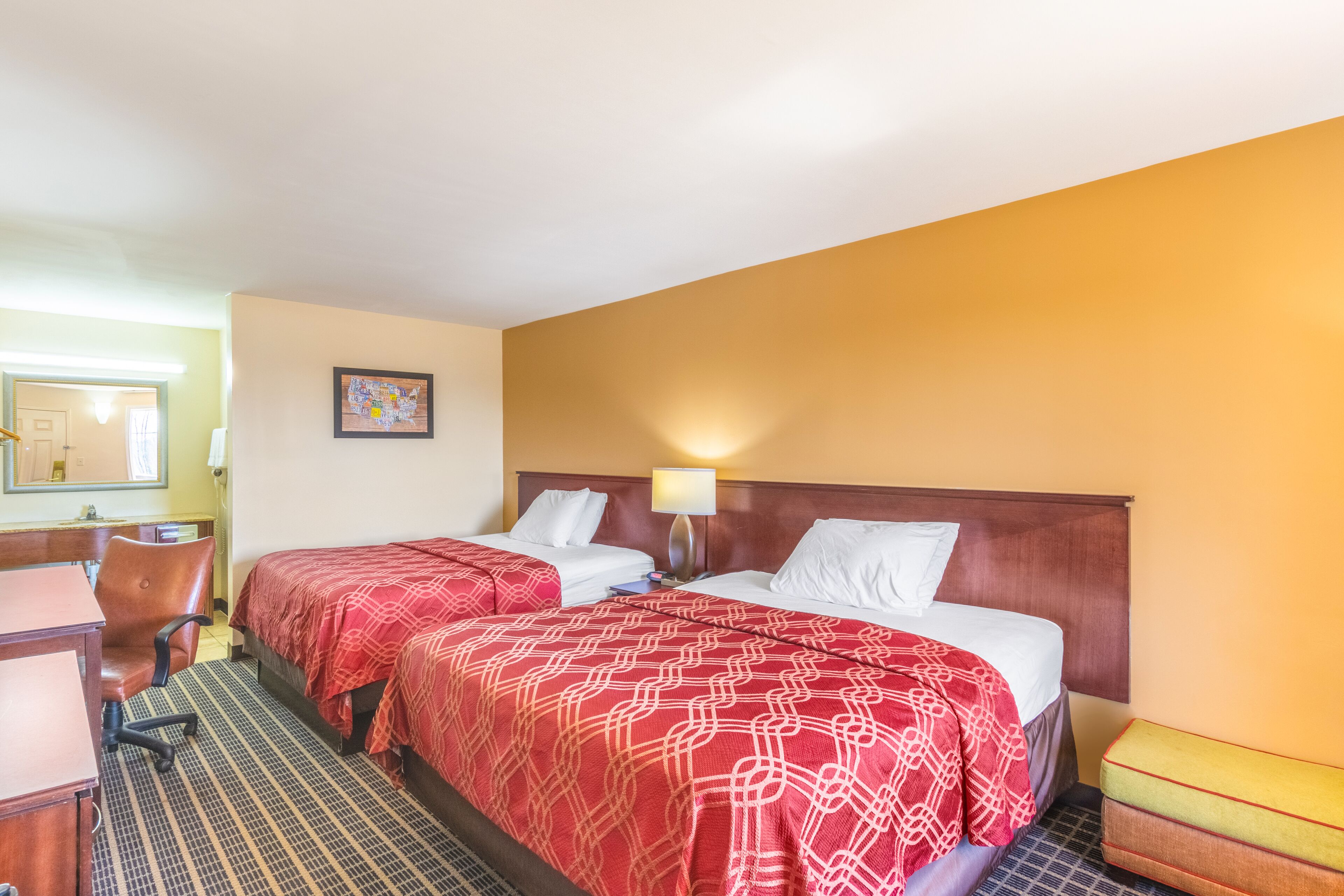 A hotel room with two beds, a desk, and a chair.