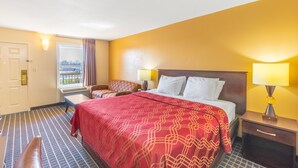 A hotel room with a large bed, two bedside tables, a window with curtains, a chair, and a view of the outside. - Econo Lodge Gaffney (Gaffney)