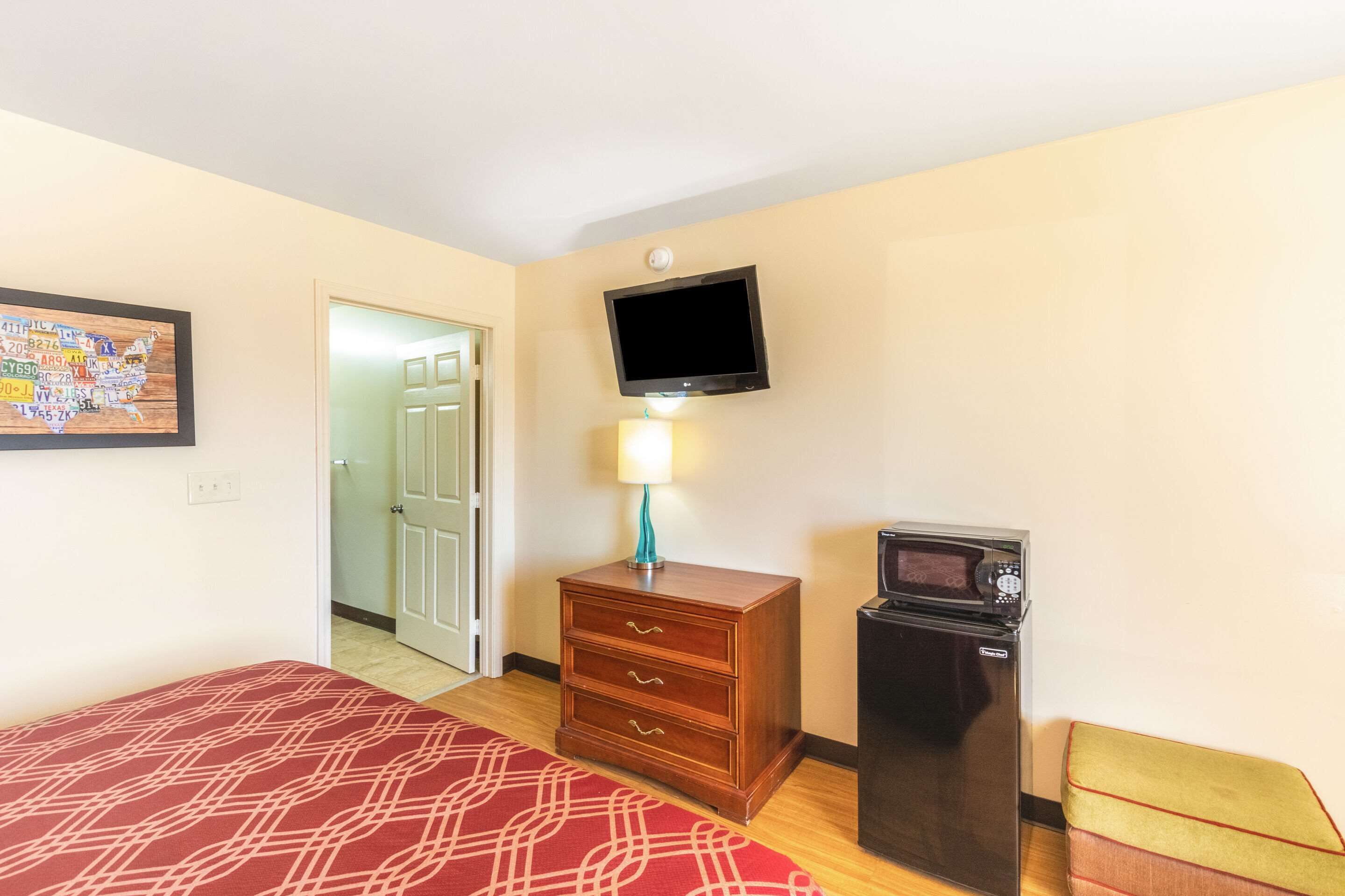A hotel room with a bed, a wooden dresser, a television, and a microwave.