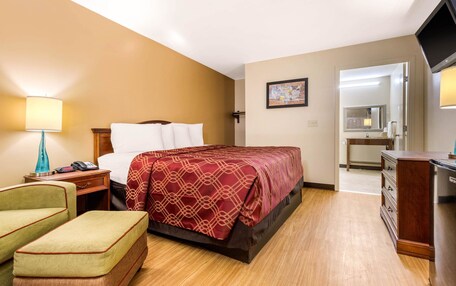 A hotel room with a bed, a desk, a chair, a TV, and a bathroom visible through an open door.