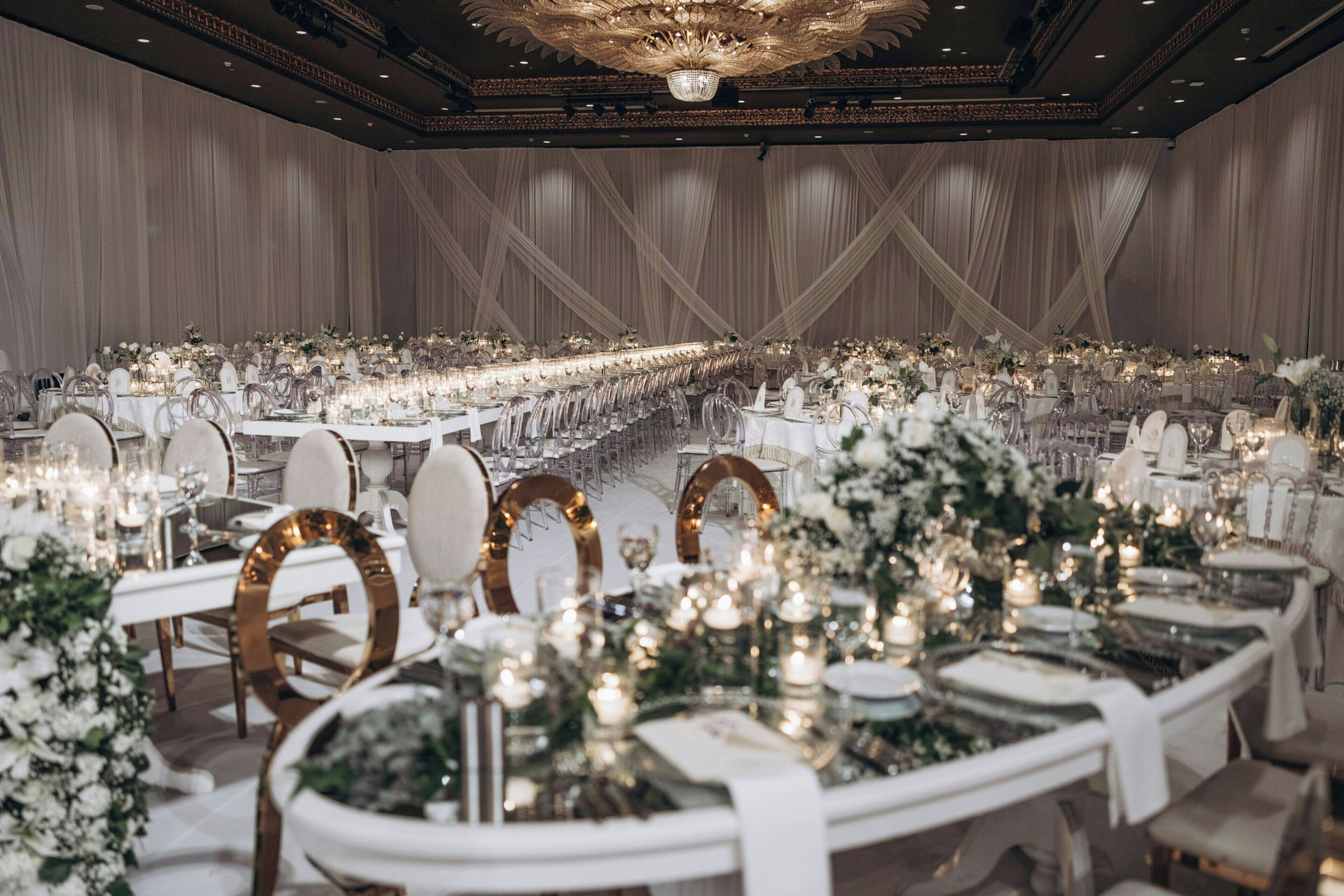 A banquet hall with long tables, elegant chandeliers, and floral centerpieces.