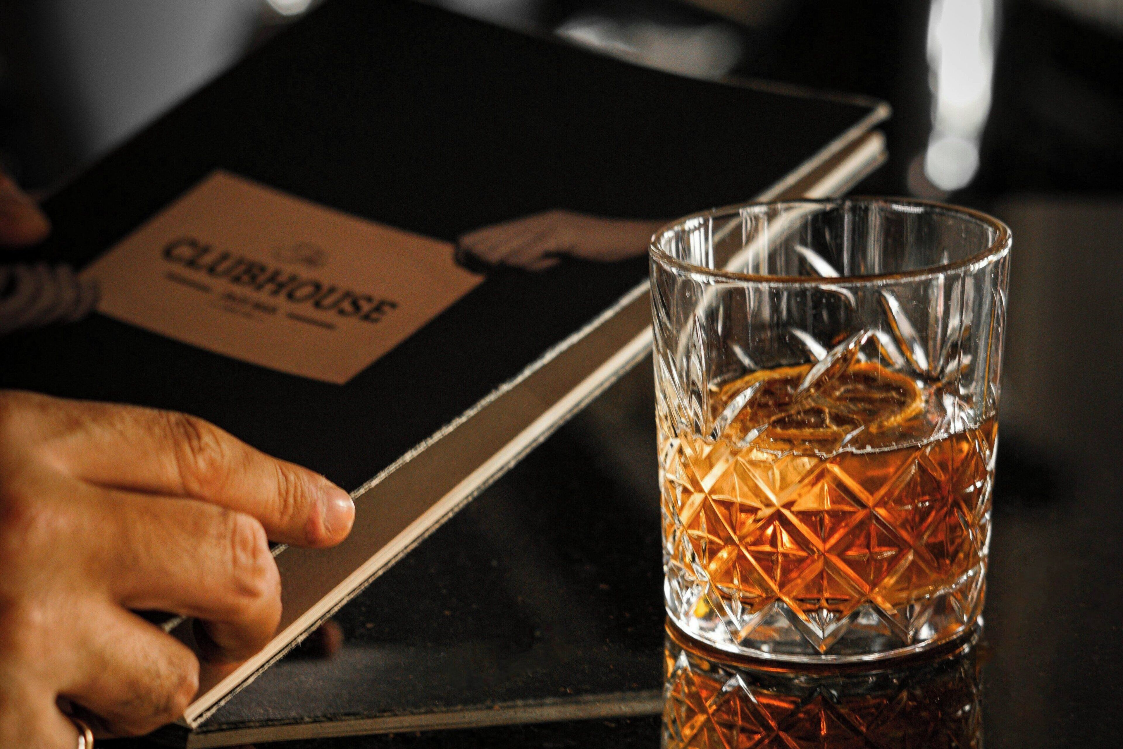 A hand holding a tablet with a 'CLUBHOUSE' label, and a glass with a geometric pattern.
