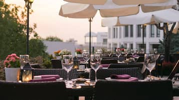 Un área de comedor al aire libre con sillas y mesas de mimbre, cada juego con copas de vino y cubiertos.