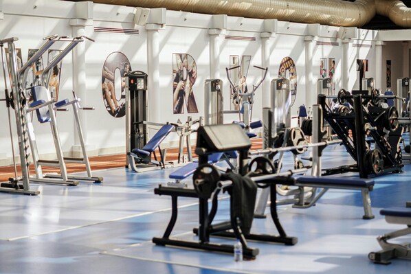 A gym with exercise equipment, mirrors, and posters on the walls.