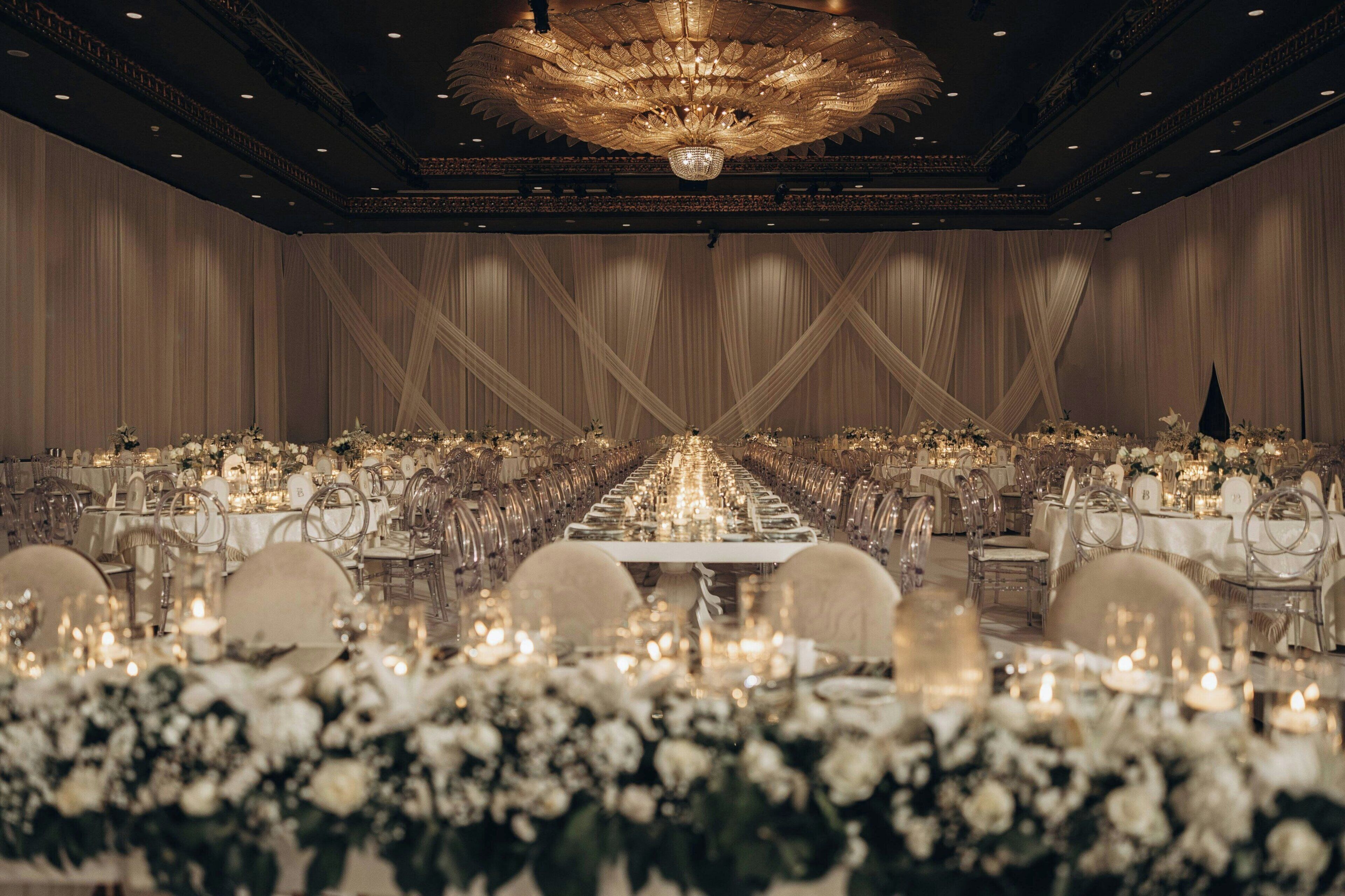 A banquet hall with long tables, chandeliers, and floral arrangements.