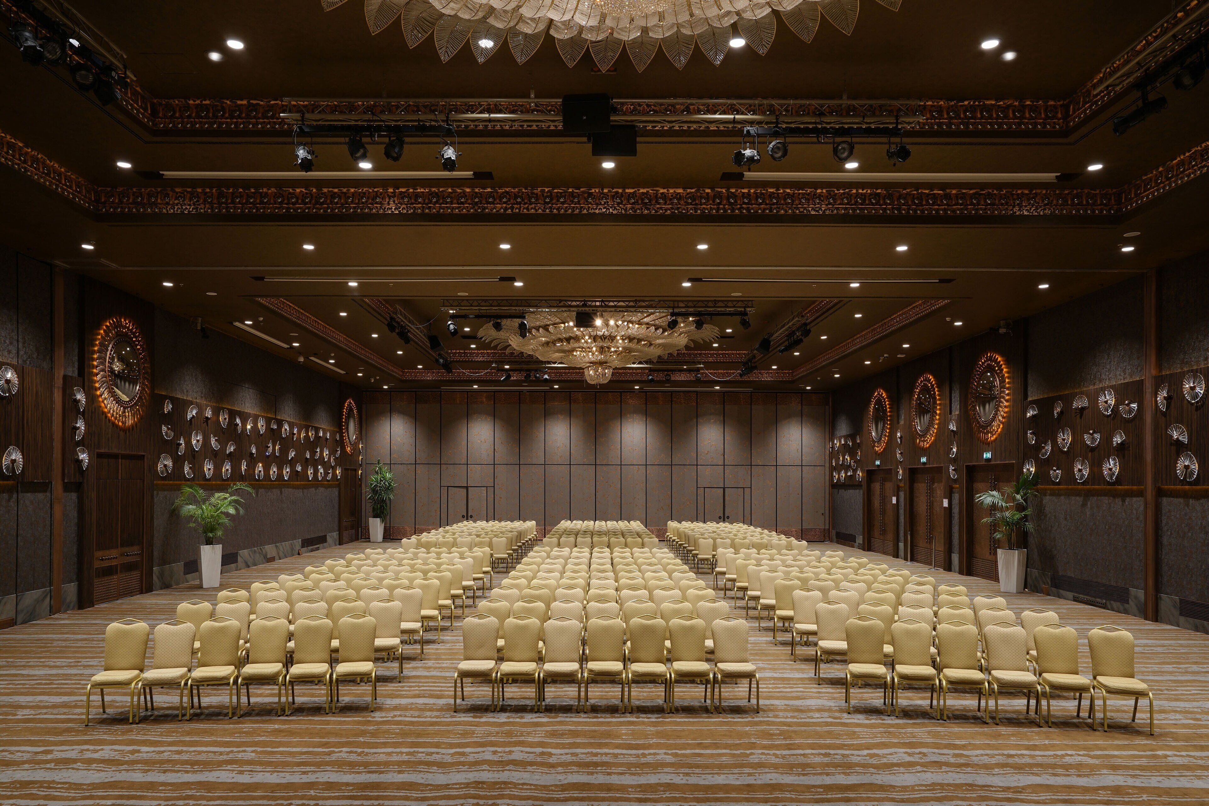 A large conference room with rows of chairs, a chandelier, and decorative wall clocks.