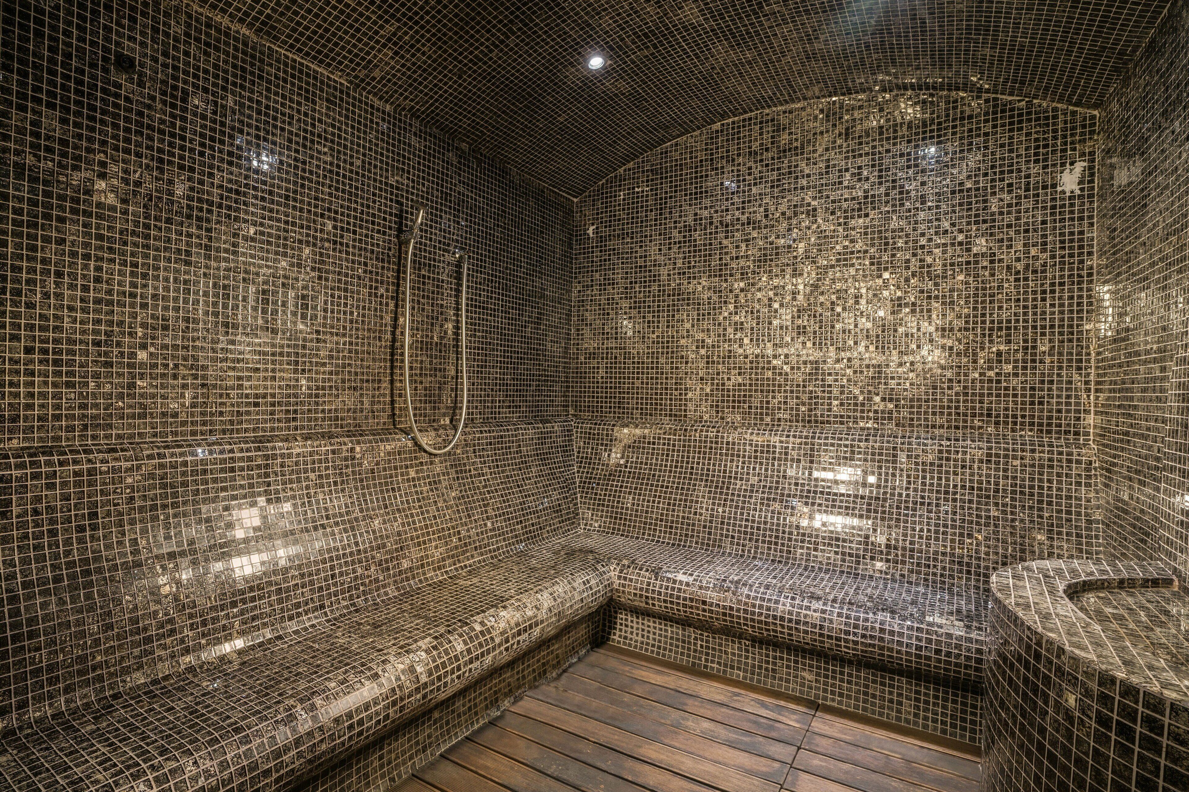 A spa room with mosaic tiled walls and a wooden floor.