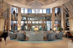 A spacious lobby with a grand chandelier, comfortable seating, and large windows offering views of the city.