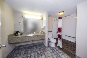 A bathroom with a granite countertop sink, a white toilet, a shower with a red and white striped curtain, and a mirror with a light above it. - Red Roof Inn Atlanta - Suwanee/ Mall of Georgia (Suwanee)