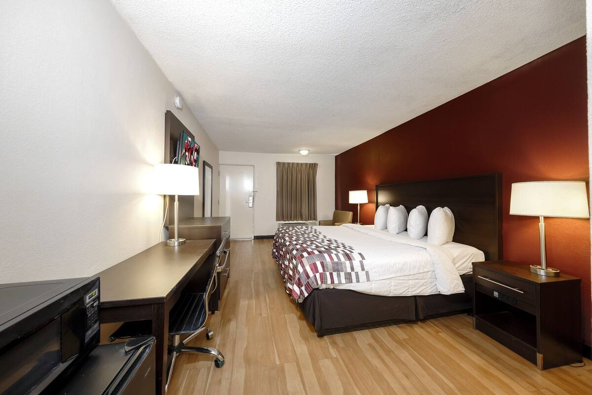 A hotel room with a bed, bedside tables, a desk, a chair, a microwave, and a television.