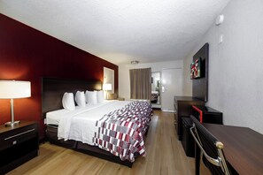 A hotel room with a bed, bedside tables, a desk, a chair, a television, and a microwave. - Red Roof Inn Atlanta - Suwanee/ Mall of Georgia (Suwanee)