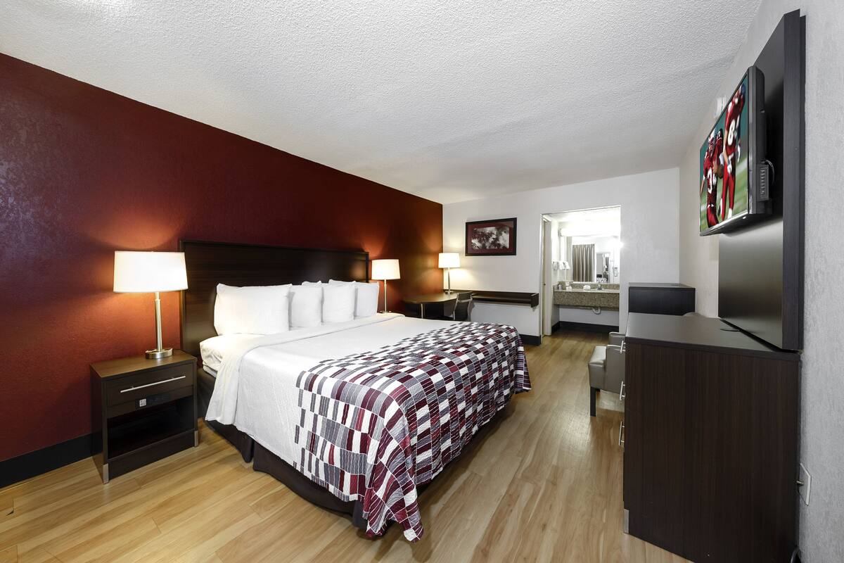 A hotel room with a large bed, two bedside tables with lamps, a flat-screen TV mounted on the wall, and a wooden floor.